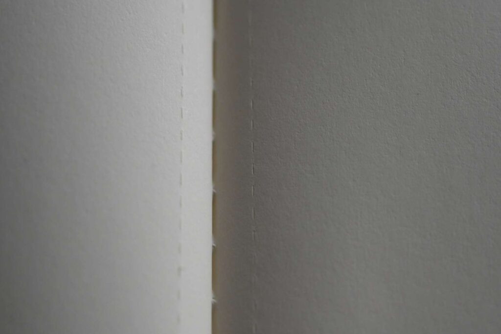 マクロレンズで接写したNASA限定版モレスキン カイエジャーナルの無地ページ。切り離し用のミシン目と、アイボリー色の中性紙の質感が自然光で鮮明に写っている。