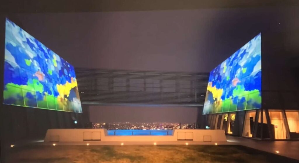 虎ノ門ヒルズ TOKYO NODE 49階 SKY GARDEN & POOLにて、インフィニティプールと夜景を背景に、壁面に投影されたワタタクの作品「童心にかえろう」の展示風景。